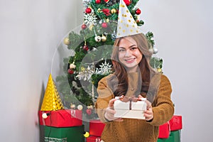 Merry Christmas and Happy Holidays! Young woman with a beautiful face in a yellow shirt shows joy with gift boxes in a house with