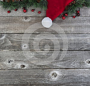 Merry Christmas or happy New Year background with fir tip branches and red white Santa Claus cap on rustic wood