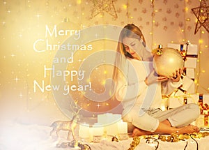 Merry Christmas and Happy New Year! beautiful young woman with long hair in knitted sweater sitting indoor decorated lights