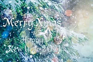 Merry Christmas and Happy New Year 2021! Blurred background of Christmas tree in snowfall decorated with silver balls, lights.