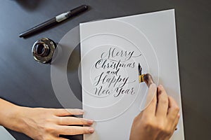 Merry christmas and a happy new year. Calligrapher Young Woman writes phrase on white paper. Inscribing ornamental