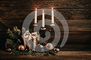 Merry Christmas and Happy New Year! Candelabra with three candles, boxes with gifts, Christmas balls and fir branches on a wooden