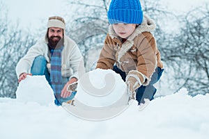 Merry Christmas and Happy New Year. Happy father and son making snowman in the snow. Handmade funny snow man.