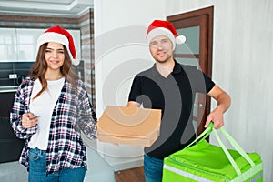 Merry christmas and happy new year. Food delivery man in red santa hat brought order to woman. They both look at the