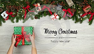 Merry Christmas and happy new year greetings in vertical top view white wood with pine branches,ribbons, lights,hands