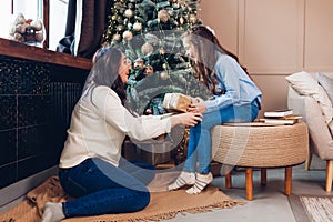 Merry Christmas and Happy New Year. Mom gives daughter present by tree at home. Happy girl laughing