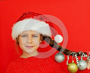 Merry Christmas and happy New year. Portrait of a beautiful smiling girl in a red dress and Santa hat, with a pigtail on