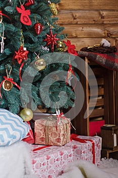 Merry Christmas and Happy New Year presents standing under the decorated fir-tree with red bulbs, toys and bows.