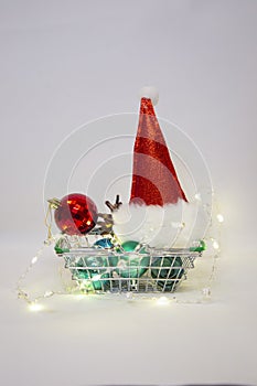 Merry Christmas and Happy New year:Santa Claus hat Christmas balls and electric garland in shopping basket vertical