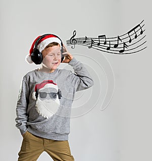Merry christmas and happy new year. School kid boy in Santa hat listening to music in headphones. Child singing