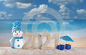 Merry Christmas and Happy New Year. Snowman and the inscription 2021 in sand on beach