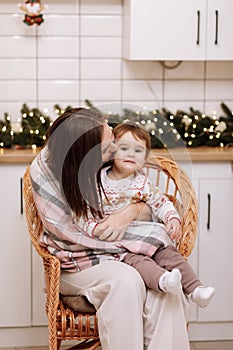 Merry Christmas and Happy New Years Holidays. Young mother hugging and kissing her baby daughter, sitting and relaxing