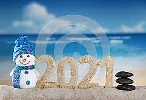 Merry Christmas. Happy snowman and lettering 2021 in sand on the beach