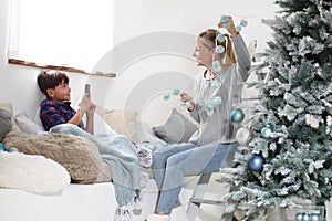 Merry christmas at home, smiling child takes a photo with mobile phone to mom while decorate the tree with balls and pine cones