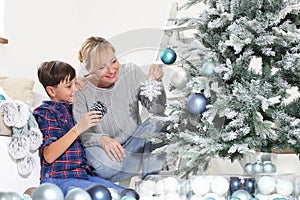 Merry christmas at home, smiling mom and son decorate tree hang decorations and balls in the living room