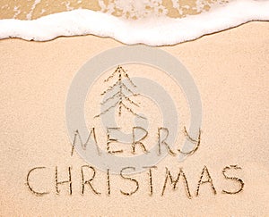 Merry Christmas inscription on wet yellow beach sand