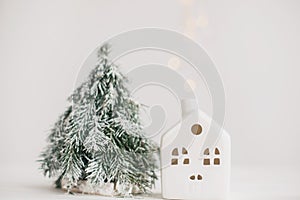 Merry Christmas. Christmas little house with golden lights bokeh and tree on white background. Happy holidays. Miniature cozy home