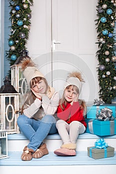 Merry Christmas! New Year. Two little girls are sitting on porch of house for Christmas. Happy children play in winter in courtyar