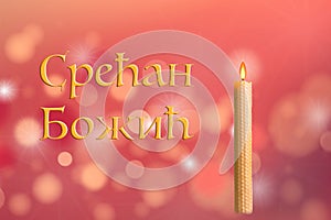 `Merry Christmas` in Serbian. Blurred background of a star lights and traditional burning wax candle. Celebration of orthodox Chri