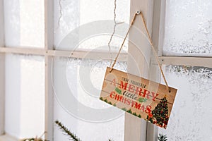 Merry Christmas sign on wall with frozen window on sunny day. Closeup of sign on door at Christmas display in home.