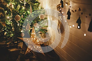 Merry Christmas! Stylish Christmas star, tree with white baubles, boho ornaments, golden lights and gifts in atmospheric evening