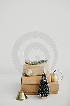 Merry Christmas! Stylish eco christmas gift boxes on white table. Simple craft christmas presents with golden baubles, tree and