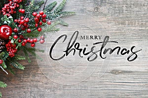 Merry Christmas Text with Christmas Evergreen Branches and Berries in Corner Over Rustic Wood Background