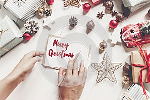 merry christmas text, seasonal greetings card sign. hands holding pencil and writing a letter wish list or greeting flat lay wit