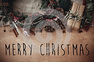 Merry Christmas text sign on stylish rustic christmas gift box with wreath, fir branches, berries, anise, pine cones, cinnamon on