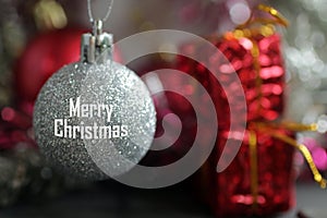 Merry Christmas text on white Christmas ball hanging on blurry background of red presents ornament. Christmas backgrounds
