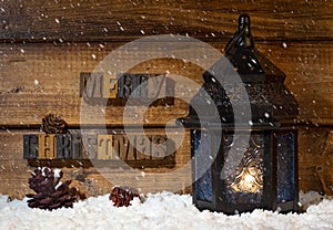 Merry Christmas text on a wooden background with burning lantern