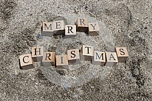 Merry christmas text from wooden cubes. The cubes are on the beach sand