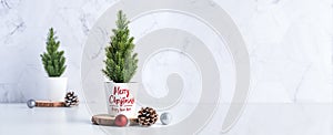 Merry christmas tree with pine cone,decor red xmas ball on wood log at white table and marble tile wall background.clean minimal