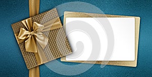 Merry christmas white gift card with golden box with ribbon bow isolated on blue glitter background, top view and copy space