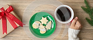 Merry Christmas with woman hand holding coffee cup and homemade cookie on table. Xmas eve, party, holiday and happy New Year