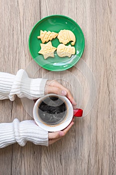 Merry Christmas with woman hand holding coffee cup and homemade cookie on table. Xmas eve, party, holiday and happy New Year