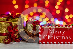 Merry Christmas wooden sign and glittery Christmas gifts. Christmas composition on blurred lights background