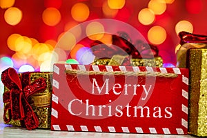 Merry Christmas wooden sign and glittery Christmas gifts. Christmas composition on blurred lights background