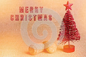 Merry Christmas written by sparkly red brush. Red artificial Christmas tree with champagne cork on bright background