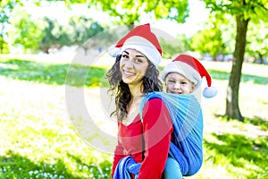 Merry christmas! Young family portrait celebrating xmas time wearing santa claus hat standing outdoors in park. mother and child