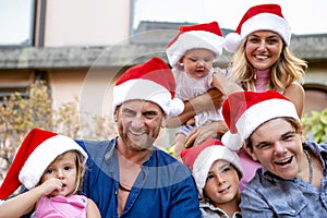 Merry christmas! young large family portrait celebrating xmas wearing a santa hat outdoors. parents and children close up during