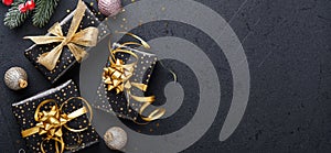 Merry Cristmas. Holiday gift box or present with ribbon, golden confetti and gold baubles on black background. Magic christmas