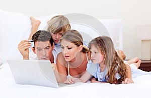 Merry family buying online lying down on bed