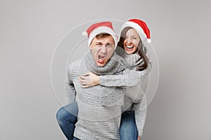 Merry fun couple girl guy in red Santa Christmas hat gray sweaters scarves isolated on grey wall background, studio