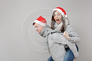 Merry fun couple girl guy in red Santa Christmas hat gray sweaters scarves isolated on grey wall background, studio