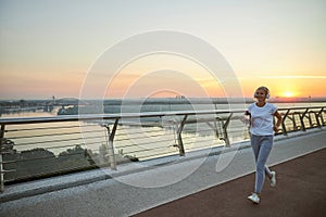 Merry lady in headphones jogging outdoors in the evening