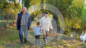 Merry old people with kid go through spring forest on fishing to river on sunny afternoon