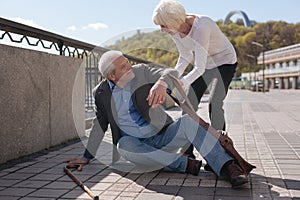 Merry pensioner sitting on the street and receiving help