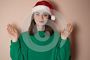 Merry surprised young woman wear xmas sweater Santa hat posing pointing hands arms aside indicate on workspace area isolated on