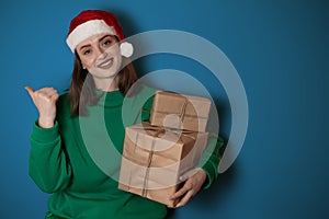 Merry surprised young woman wear xmas sweater Santa hat posing pointing hands arms aside indicate on workspace area isolated on